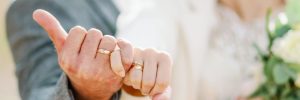 a romantic close-up of a bride and groom linking pinky fingers, showing their wedding rings in soft natural light.