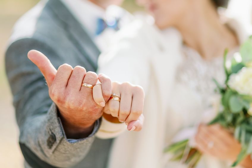a romantic close-up of a bride and groom linking pinky fingers, showing their wedding rings in soft natural light.
